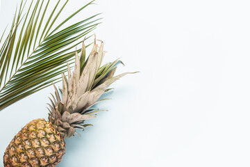 whole ripe pineapple and a leaf of a palm tree on a light background. Top view, flat lay