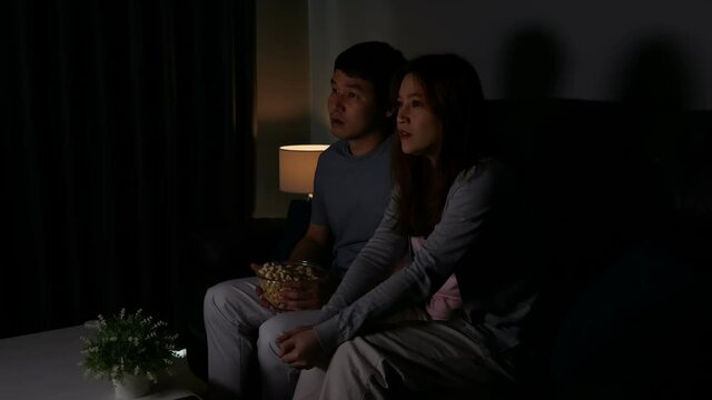 Young scared couple is watching horror movie TV on sofa at night
