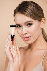 Fototapeta premium sensual woman with perfect skin showing tube of face foundation isolated on beige.