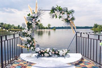 hexagonal wedding arch decorated with artificial flowers on the pier. wedding decor by the river