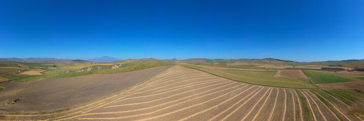 Fototapeta premium 180 degree saerial photo of the wheat fields in the heart of Sicily in the Erei mountains. Sicilian wheat cultivation. Small rural villages of Ramacca and Raddusa. Hay and grain. Etna view.