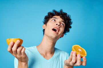 Cheerful man with curly hair holding oranges fruit blue background