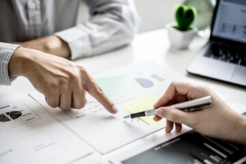 Two business partners are brainstorming on planning, managing and solving company problems, they are pointing at the company financial documents. The concept of business management for growth.