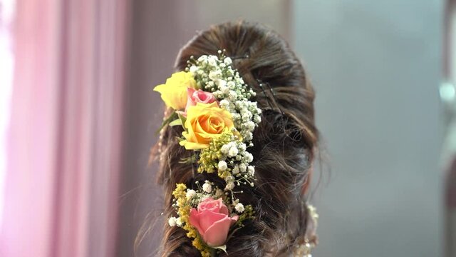 Indian wedding bride&rsquo;s hair decorated with red & yellow roses. French elegant braid bridal hairstyle & makeup at Indian festive ceremony.
