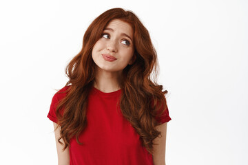 Indecisive cute redhead woman looking aside, avoid eye contact and shrugging unsure, hesitating, standing coy in t-shirt against white background