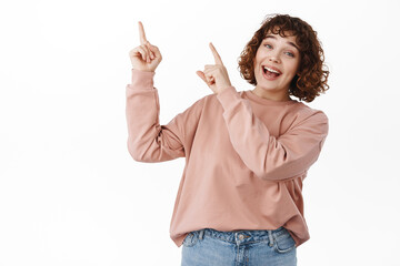 Hey check it out, click here. Smiling cute girl pointing fingers at upper left corner, top...
