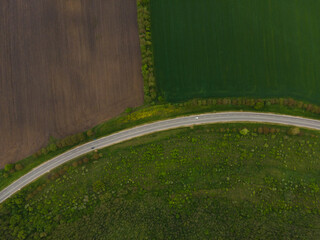Top view of green fields and road with cars moving along the highway. Photo from drone.