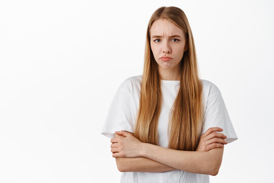 Image of angry offended blond girl, sulking and frowning upset about unfair thing, cross arms on chest and pouting disappointed, standing over white background