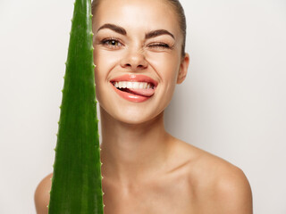 cheerful woman with aloe leaf shows her tongue and laughs on a light background