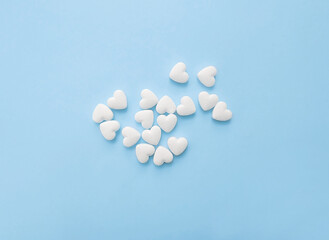 Fototapeta na wymiar White pills in the shape of hearts on a pastel blue background