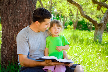happy father with a child reading a book on the nature of the Bible