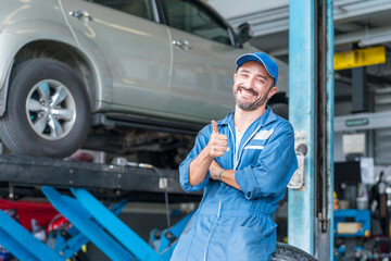 Car repairs. Happy auto mechanic man or smith at car workshop. A car mechanic showing his thumb up.