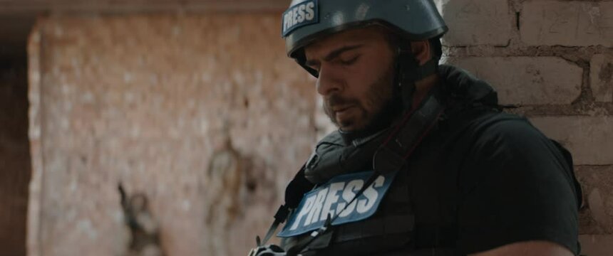 Hispanic male war journalist wearing protective helmet and bulletproof vest gear taking photos during military operation. Shot with 2x anamorphic lens