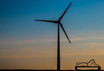 A windmill and a man statue laying next to that at Sunrise. Near Goliath old windmill near...