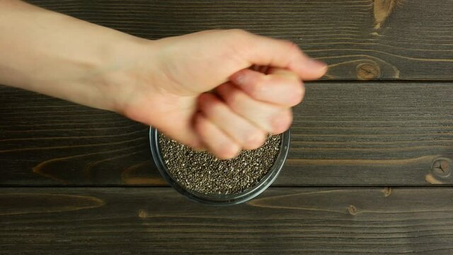 Hand pours chia seeds. Falling chia seeds. Rustic wooden table. Top view, flat lay. 4k video.