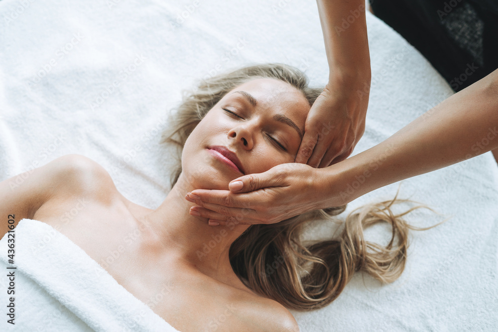 Wall mural attractive blonde young woman on couch with white linen enjoys hand facial massage in the spa, treat