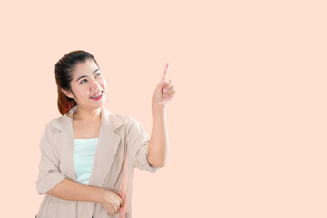 A young Asian woman standing, pointing the index finger of her left hand upward with a smiling face.