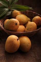 Mango fruits in wooden basket with leaf after harvest from farm, Mango fruits with leaf on Jute background.