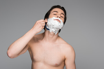 young man with foam shaving with safety razor isolated on grey.