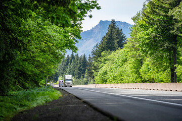 Convoy of different loaded big rigs semi trucks with semi trailers climbing uphill on the forested...