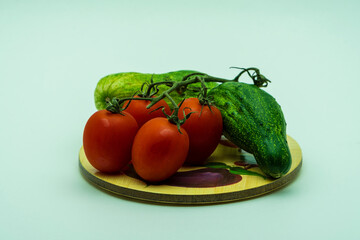Four red tomatoes and green deformed cucumber lie on the wood stand on the white background....