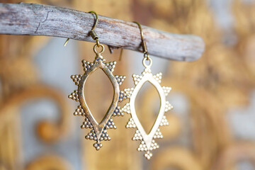 Brass metal earrings in ornamental shape hanging on neutral background - 436327417