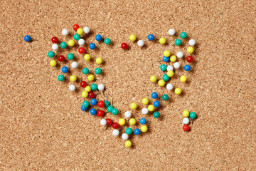 Push pins on cork board. Shape of the heart (symbol of love) is assembled from office buttons.