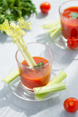  Two glasses with fresh tomato juice, celery, parsley and ripe tomatoes on light wood background