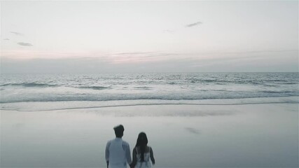 Young couple, hand in hand walking on beach at evening.  Aerial. View from back. 