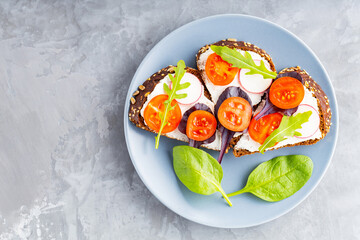 Delicious toasted sandwiches with cream cheese, cherry tomatoes and radish on gray plate. Sandwiches with cream cheese and fresh herbs on gray background. Copy space. Top view
