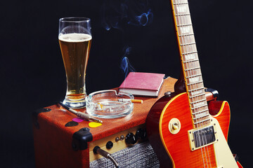 Guitar combo amplifier with guitar, glass of beer and smoking cigarette on black background.