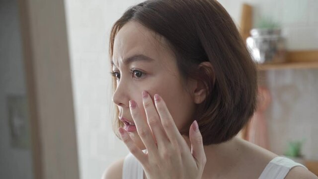 attractive beautiful short hair asian woman worry looking into mirror for face skin care condition. Frustrated Young female Examining Her Face While Looking At The Mirror in bathroom. annoy facial age