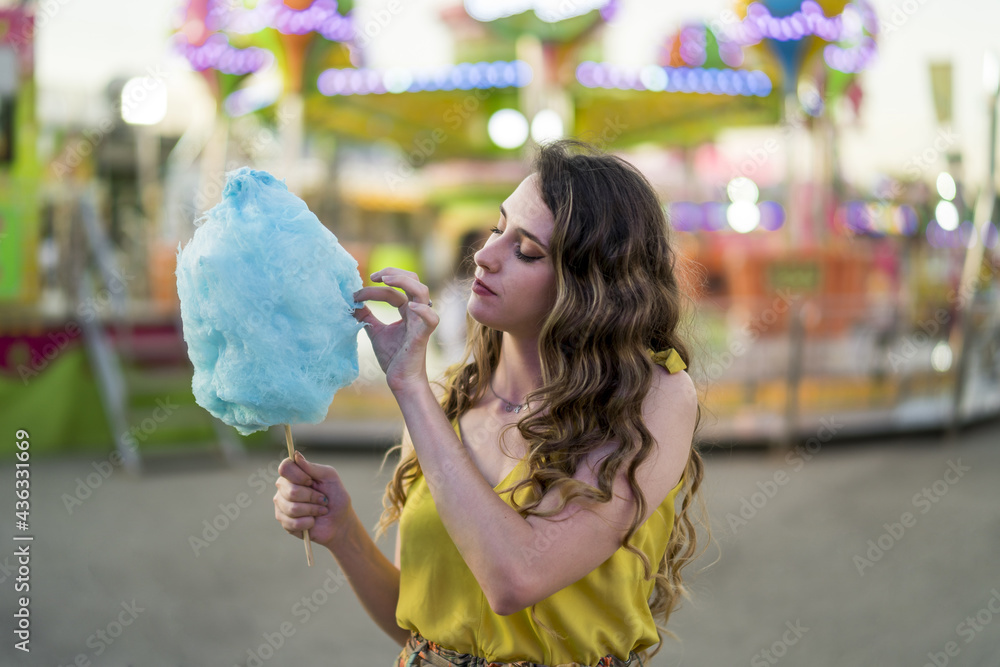 Wall mural Attractive young female standing with cotton candy in hand and spending time in an amusement park