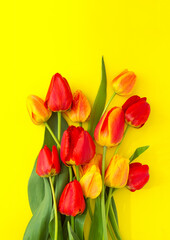 A bouquet of red and yellow tulips on a yellow background. Vertical background. Mother's Day, Valentine's Day, Birthday celebration concept. Hello spring, copy location, top view, greeting card