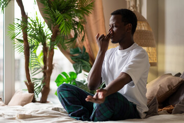 Young african man practicing yoga lesson, doing Alternate Nostril Breathing exercise