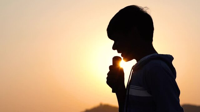 Silhouette of an Indian teen giving speech in front of the sun. Leader concept, Kid gives speech with sun in background 