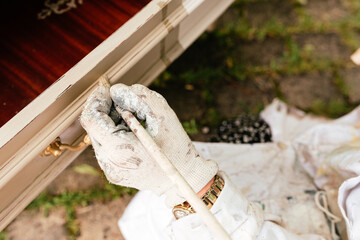 detail of hand with dirty glove painting with a brush and repairing an old wooden furniture. small...