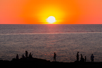 Fototapeta premium People stand on the rocky shore at sunset. Travel concept.