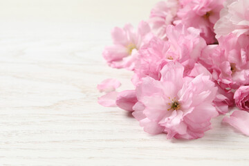 Fototapeta na wymiar Beautiful sakura tree blossoms on white wooden table, closeup. Space for text