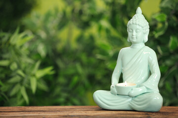 Buddha statue with burning candle on wooden table. Space for text