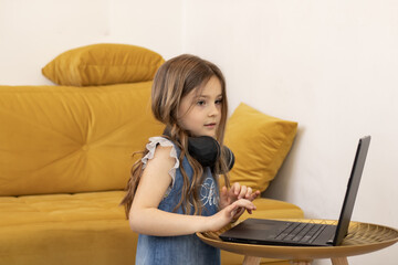 Cute little girl with headphones on her neck watching a video on a laptop