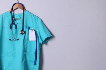 Turquoise doctor shirt with stethoscope, badge and pen hanging on light grey background. Space for...