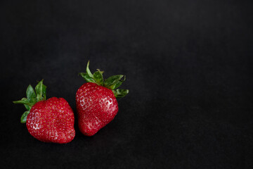 Two ripe red strawberries on black background