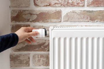 Woman adjusting thermostat of white radiator at home - obrazy, fototapety, plakaty