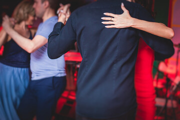 Couples dancing traditional latin argentinian dance milonga in the ballroom, tango salsa bachata kizomba lesson in the red, purple and violet lights, dance festival - obrazy, fototapety, plakaty
