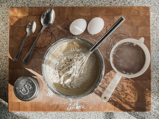 Top view of a wooden board with ingredients for making pancake dough. Composition with kitchen utensils, eggs, salt and flour. Cooking concept.