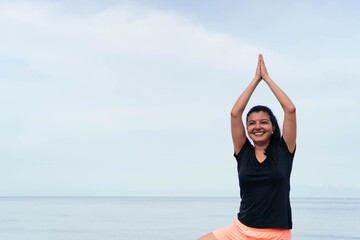 Fototapeta na wymiar Hispanic woman practicing yoga, stretching her body on the beach