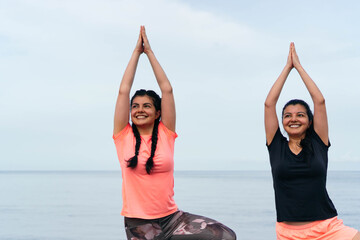 Two Latin women practicing yoga, stretching their bodies on the beach.