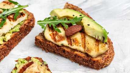 Grilled Halloumi cheese, avocado guacamole, arugula on roasted bread. Food recipe background. Close up