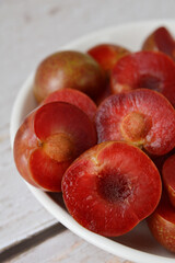 Close up half cut of delicious Vietnamese red plums with pits on plate.